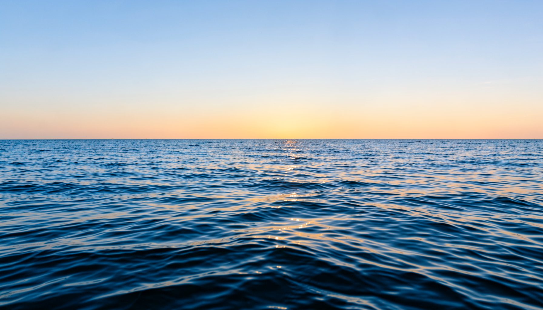 Ruhiges blaues Meer mit sanften Wellen unter einem klaren Himmel, warmes Sonnenlicht spiegelt sich auf der Wasseroberfläche