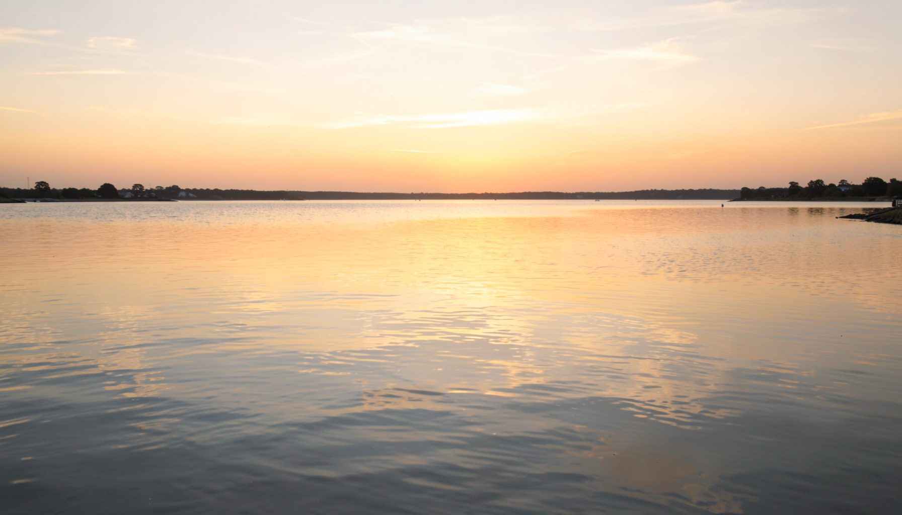 Weite Meeresbucht bei Sonnenuntergang mit ruhigem Wasser und sanftem goldenem Licht, das sich auf der Oberfläche spiegelt